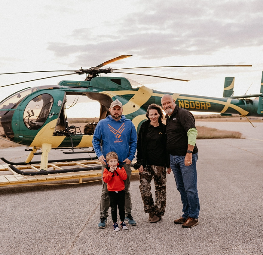 Family of four posing in front of a helicopter at sunset