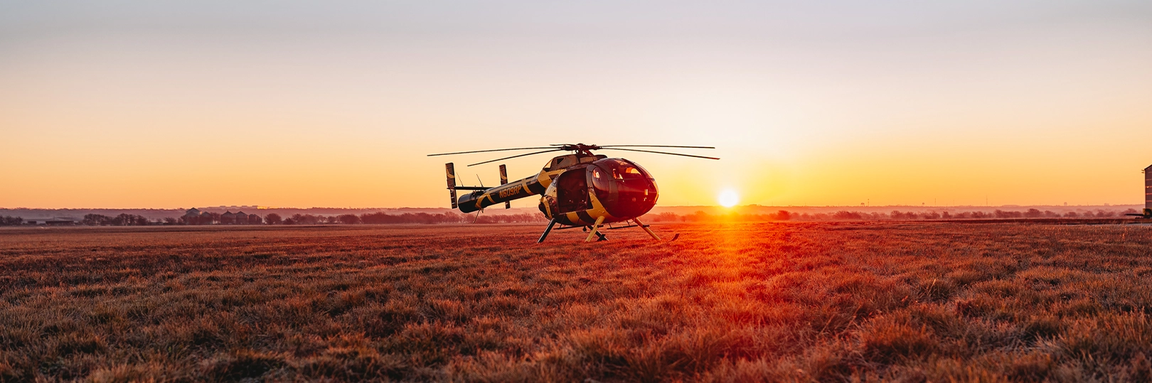 Black and yellow helicopter N609RP parked in a field as the sun rises on the horizon.