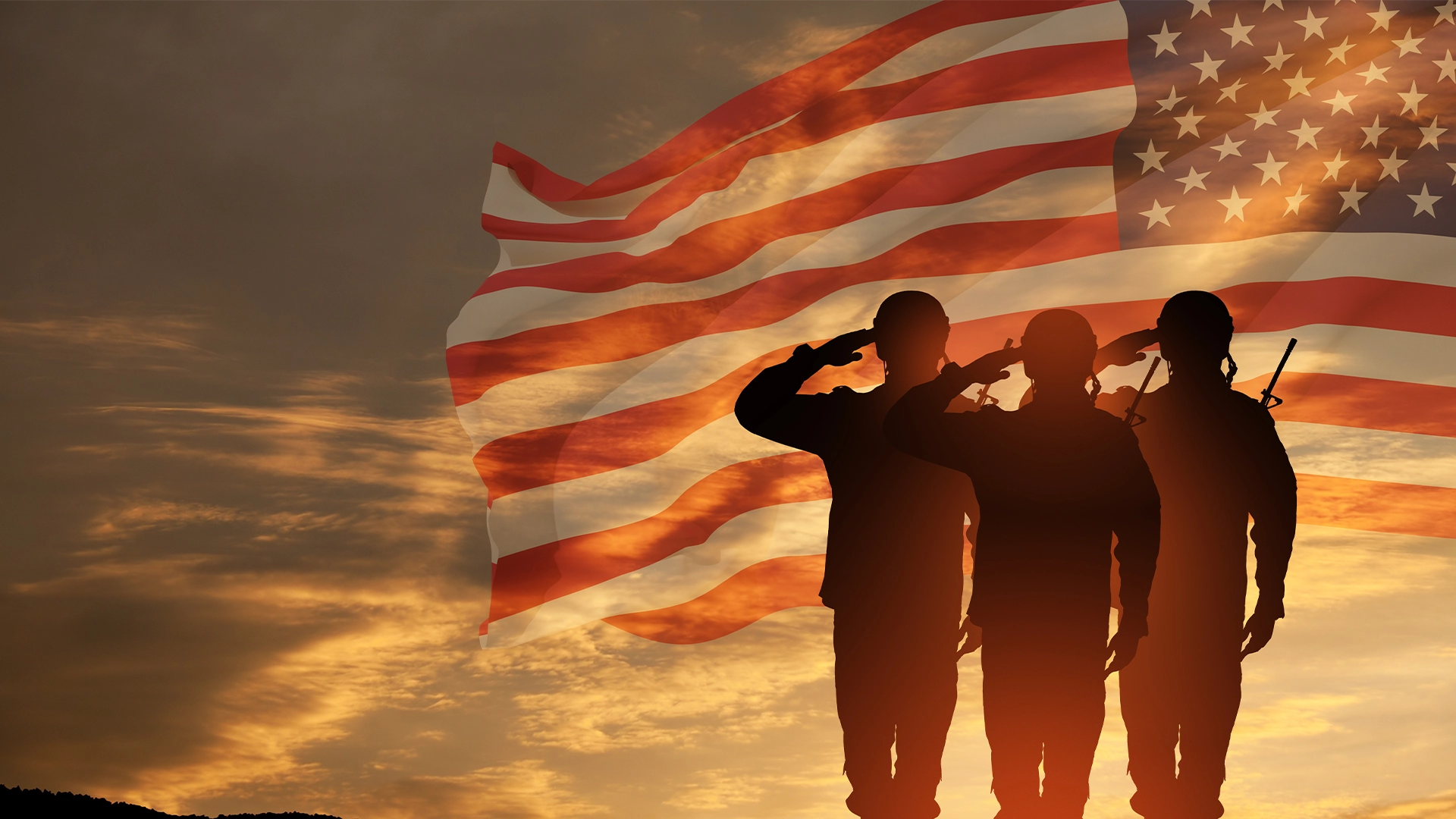 Silhouettes of three saluting soldiers against an American flag and a sunset sky.