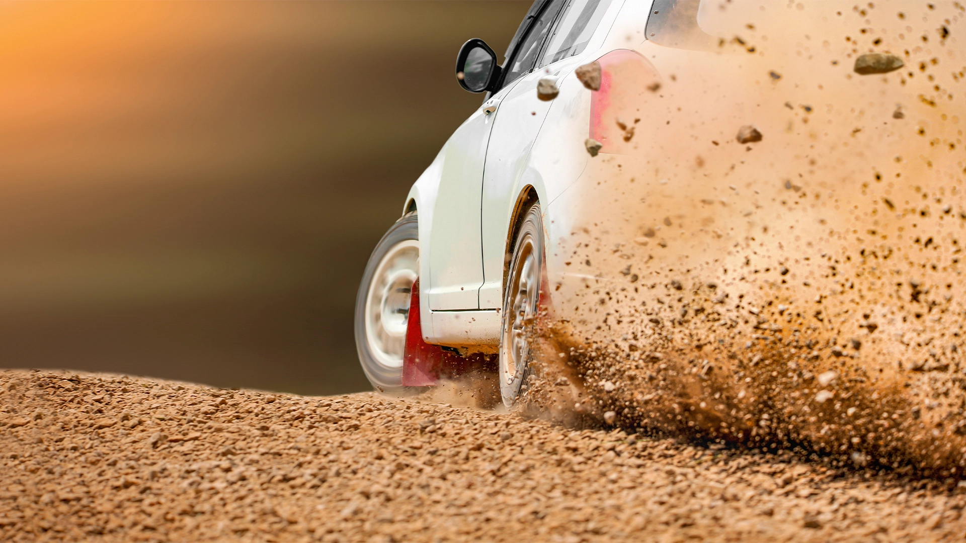 White rally car speeding along a dirt track, kicking up a spray of gravel and dust.